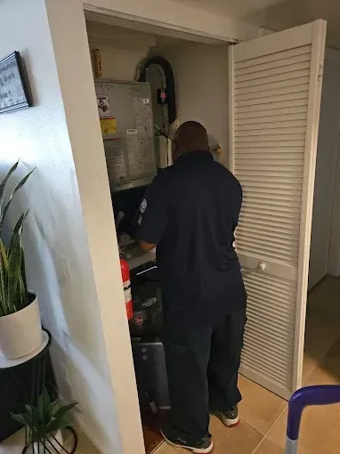 Person inspecting a utility cabinet with exposed pipes in a home hallway