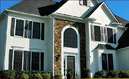 White two-story house with black shutters, stone facade around the front door, and a black roof.