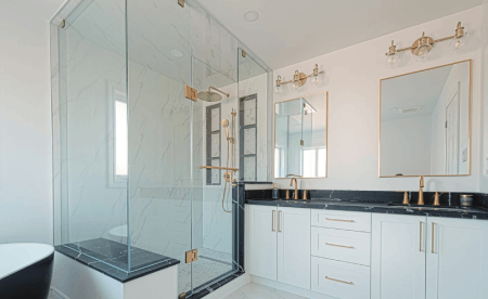 Modern white bathroom with a glass shower, gold fixtures, and a black countertop.