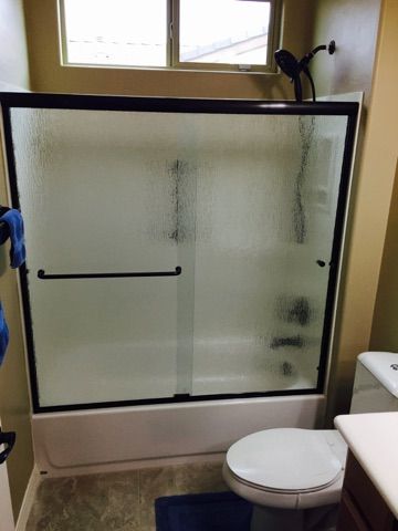Bathroom with frosted glass shower door, black frame, toilet, and a window.