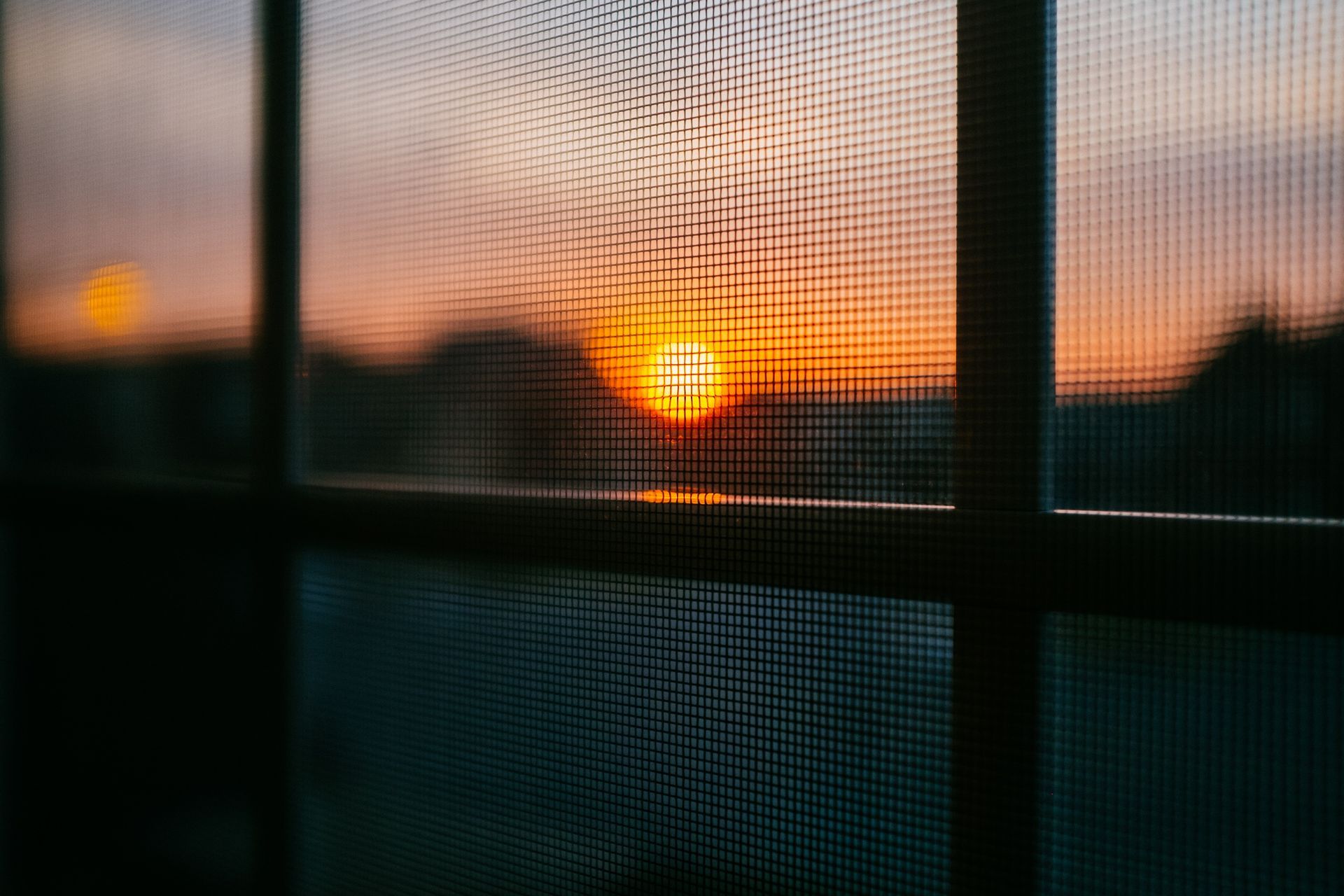 Sunset viewed through a window screen; orange and yellow sky, dark silhouettes.