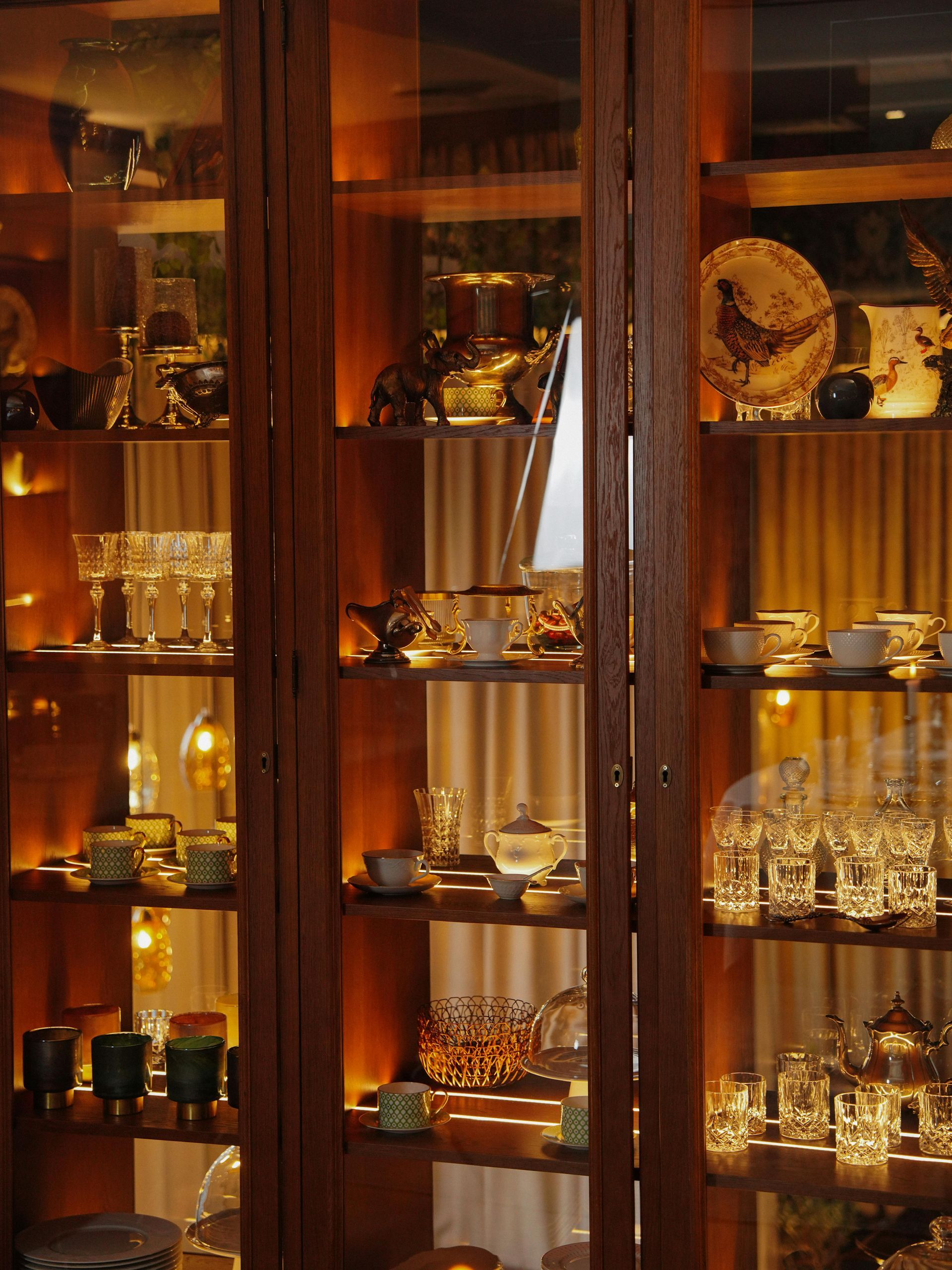 Wooden display cabinet with lit shelves holding various dishware.