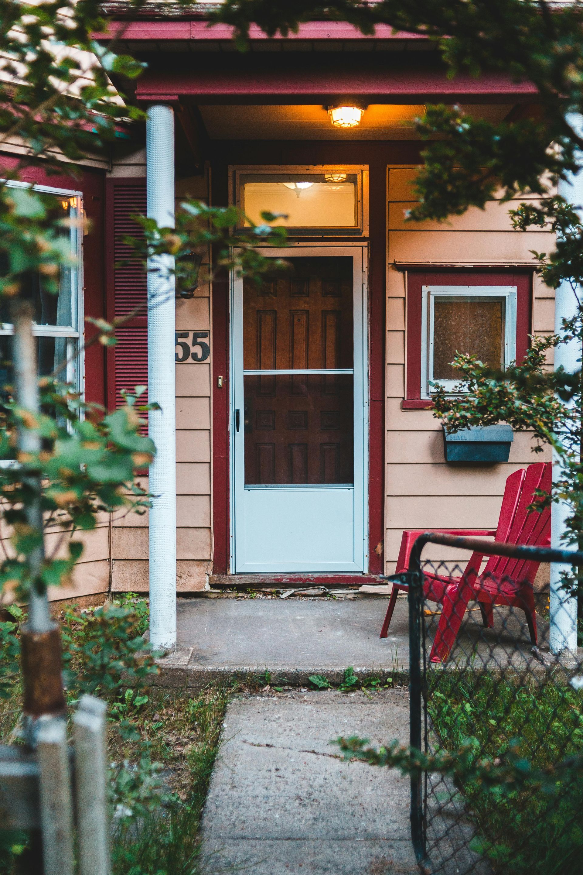 Small, tan house with red trim, a white door, and red chair on the porch.