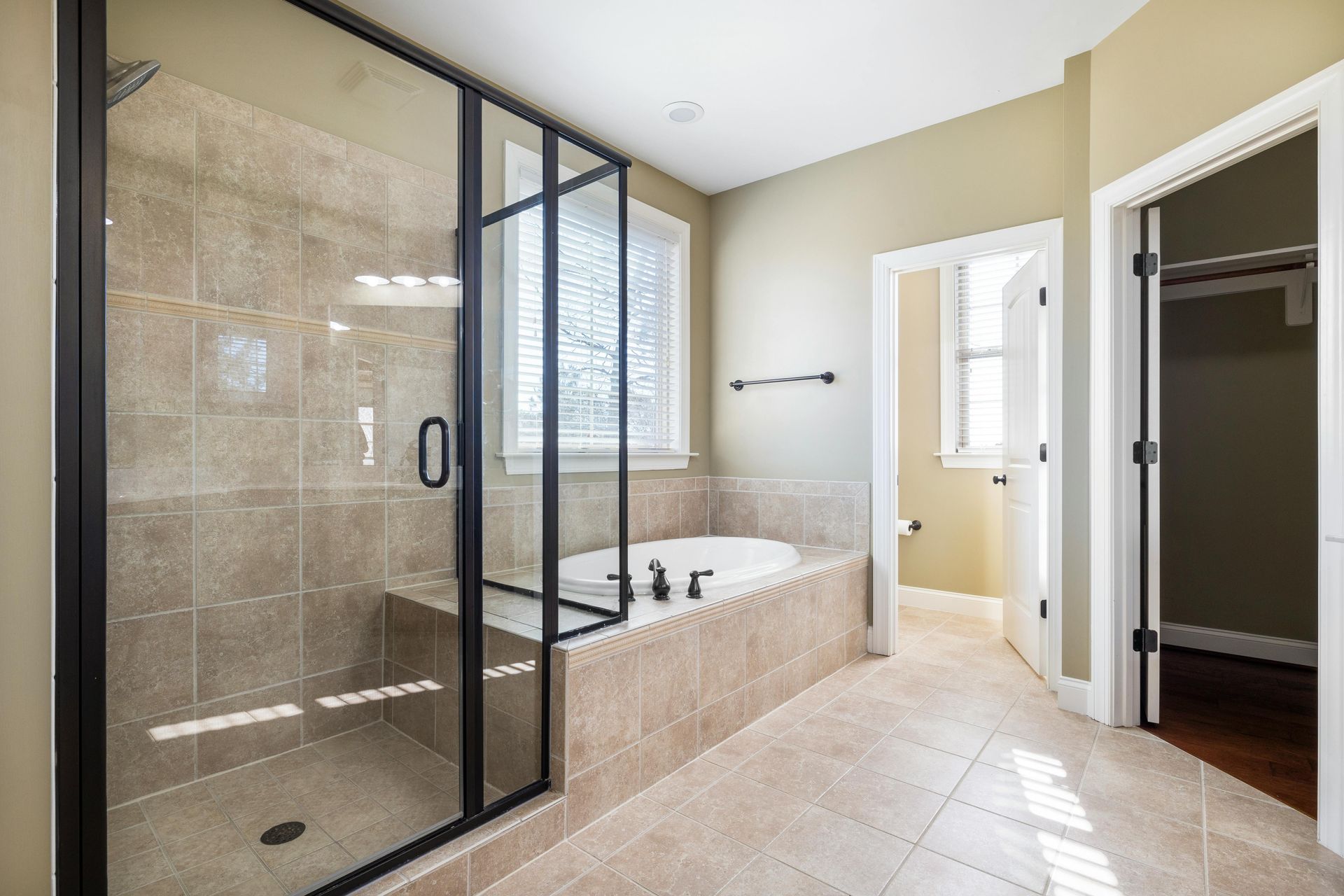 Bathroom with glass shower, soaking tub, neutral tile, and a walk-in closet doorway.
