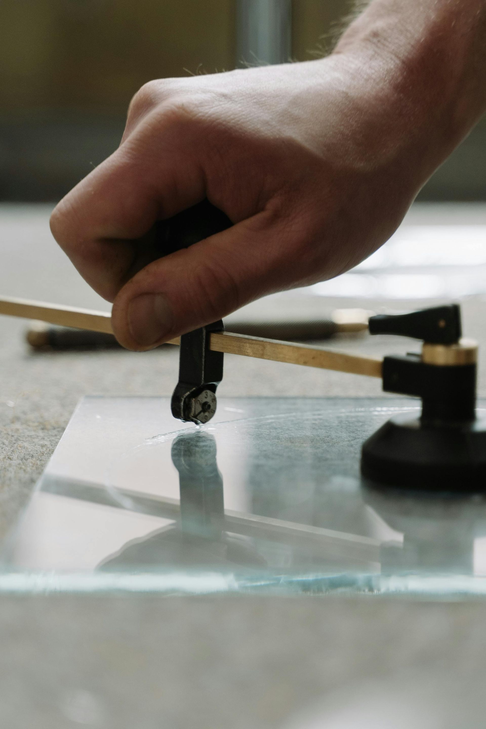 Hand using a circle cutter on a sheet of glass, preparing to cut a circle.