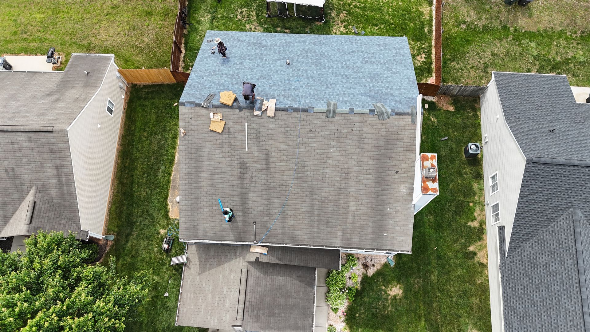 Aerial view of a house with roofers replacing shingles.  The roof is partially covered in blue shingles.