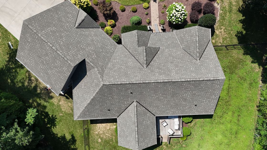 Overhead view of a gray-roofed house with multiple gables, surrounded by green lawn and landscaping.
