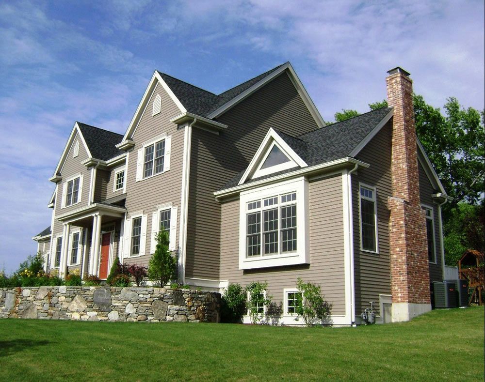 Large two-story house with tan siding, white trim, brick chimney, and green lawn under a blue sky.
