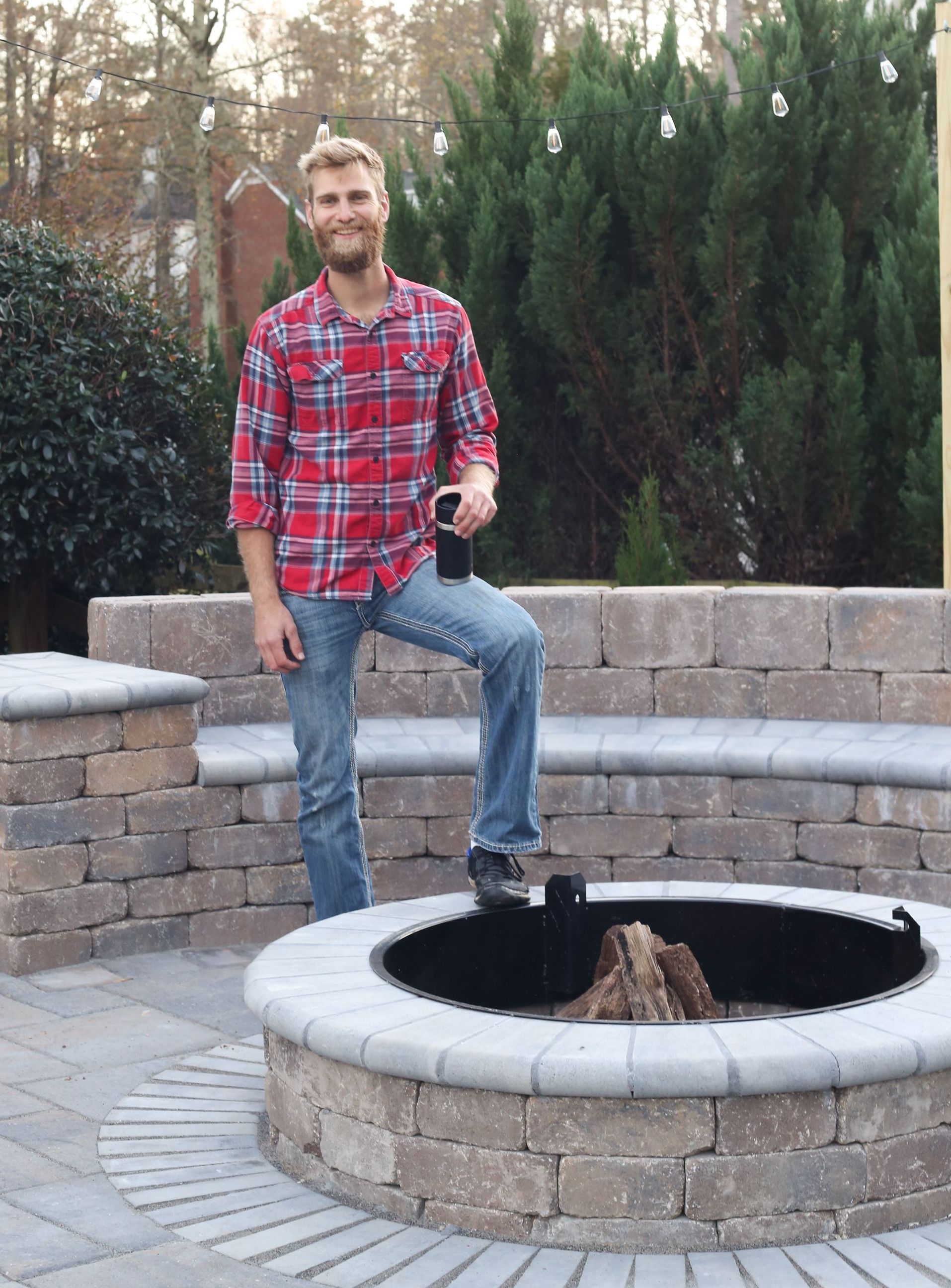 A man in a plaid shirt is standing next to a fire pit