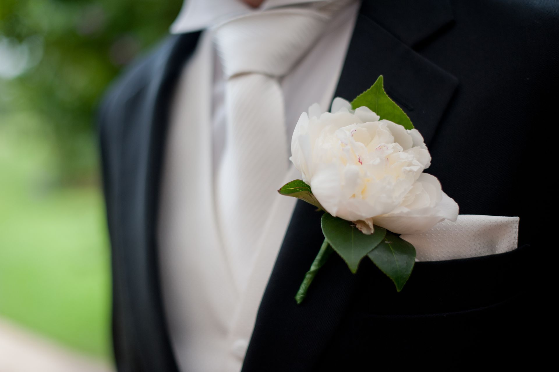 Un uomo in giacca e cravatta ha un fiore bianco in tasca.