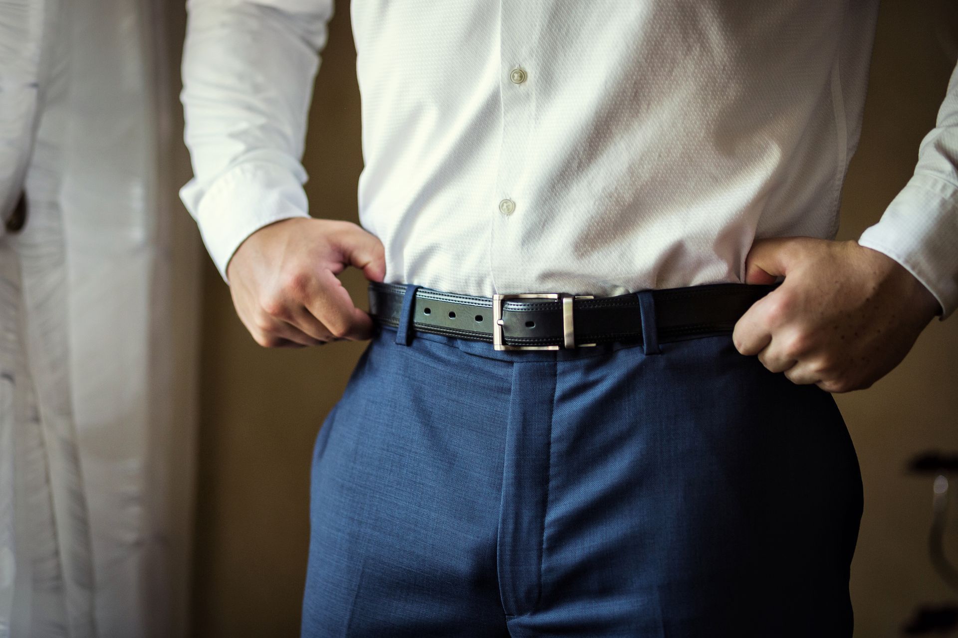 Un uomo con una camicia bianca e pantaloni blu si sta sistemando la cintura.