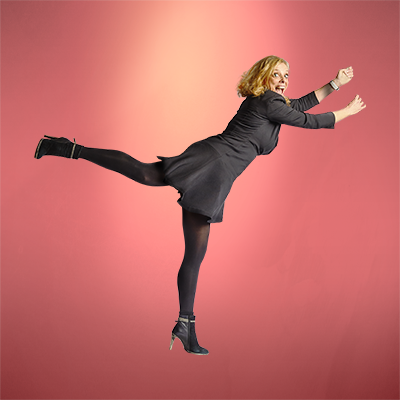 een vrouw in een zwarte jurk en zwarte panty staat op één been.