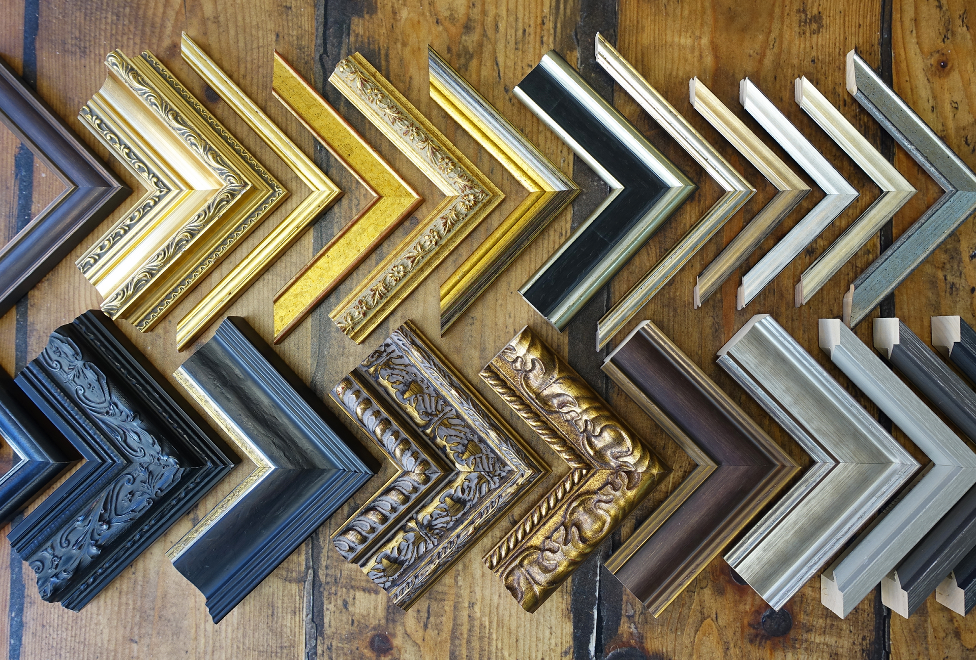 A variety of picture frames are lined up on a wooden table. Made-to-measure frames.