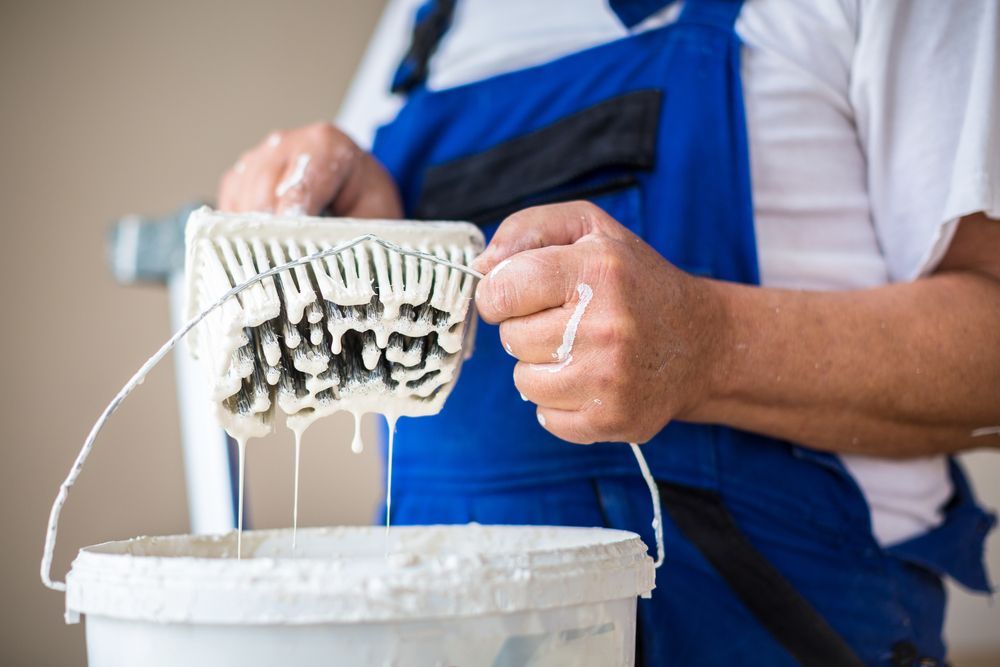 A man is pouring paint from a roller into a bucket.