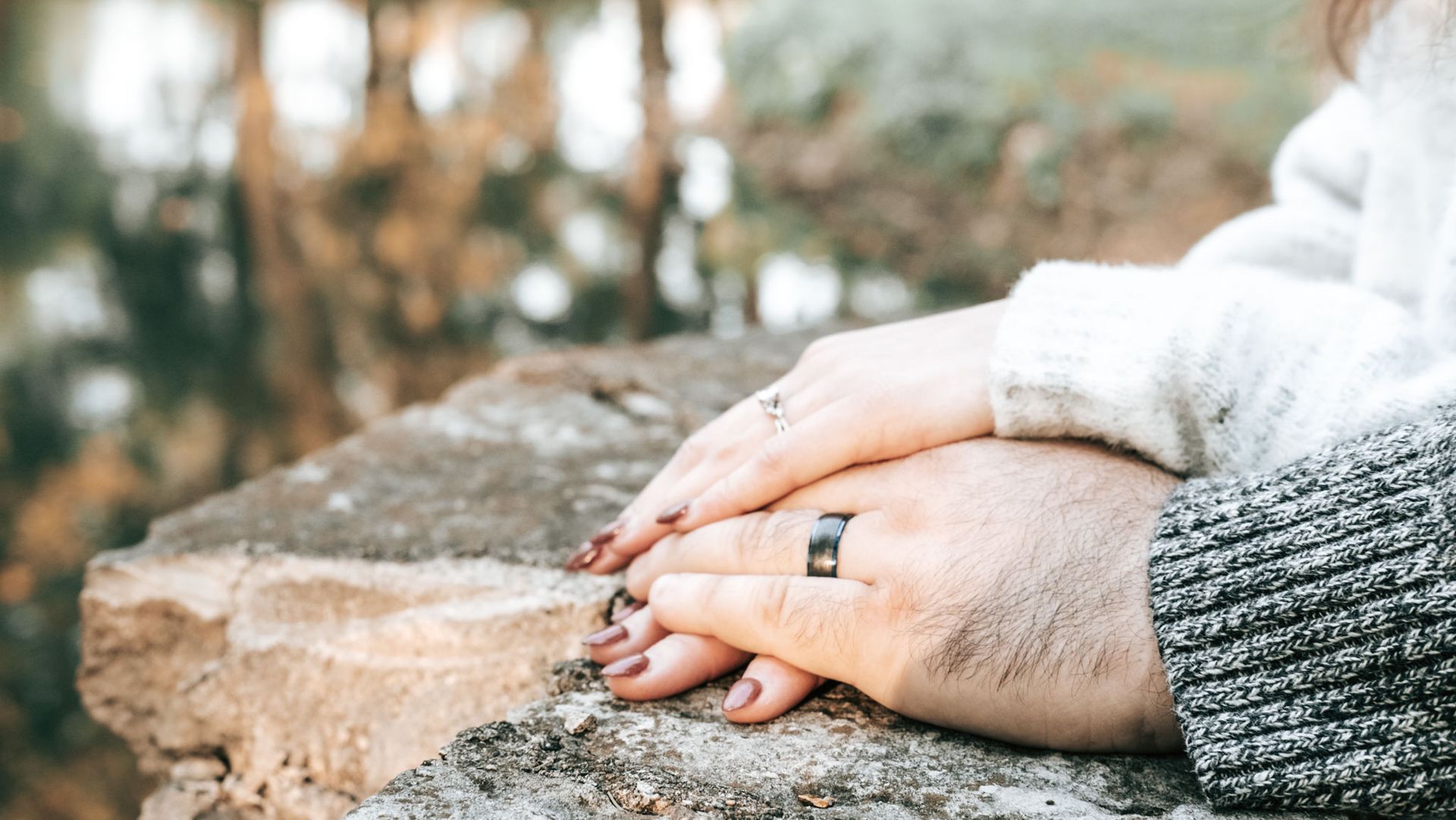 Hands resting on a stone ledge outdoors, one wearing a ring and gray sweater cuffs.