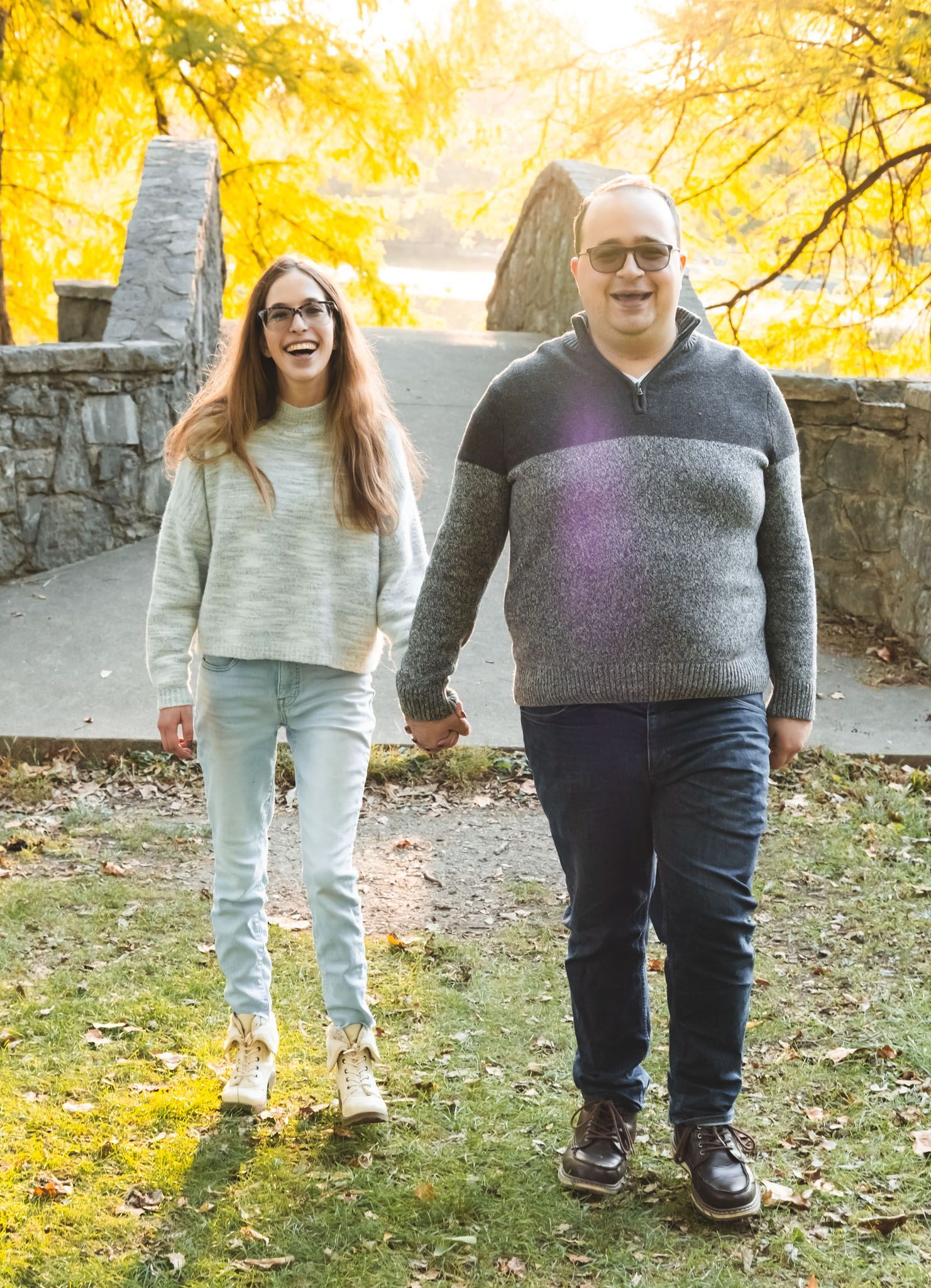 Two people walking outdoors on a path lined with yellow autumn trees.