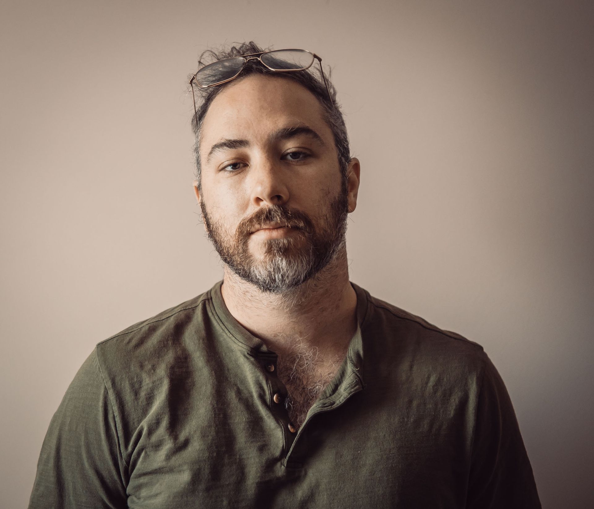 Portrait of a bearded person in a green shirt against a plain beige background