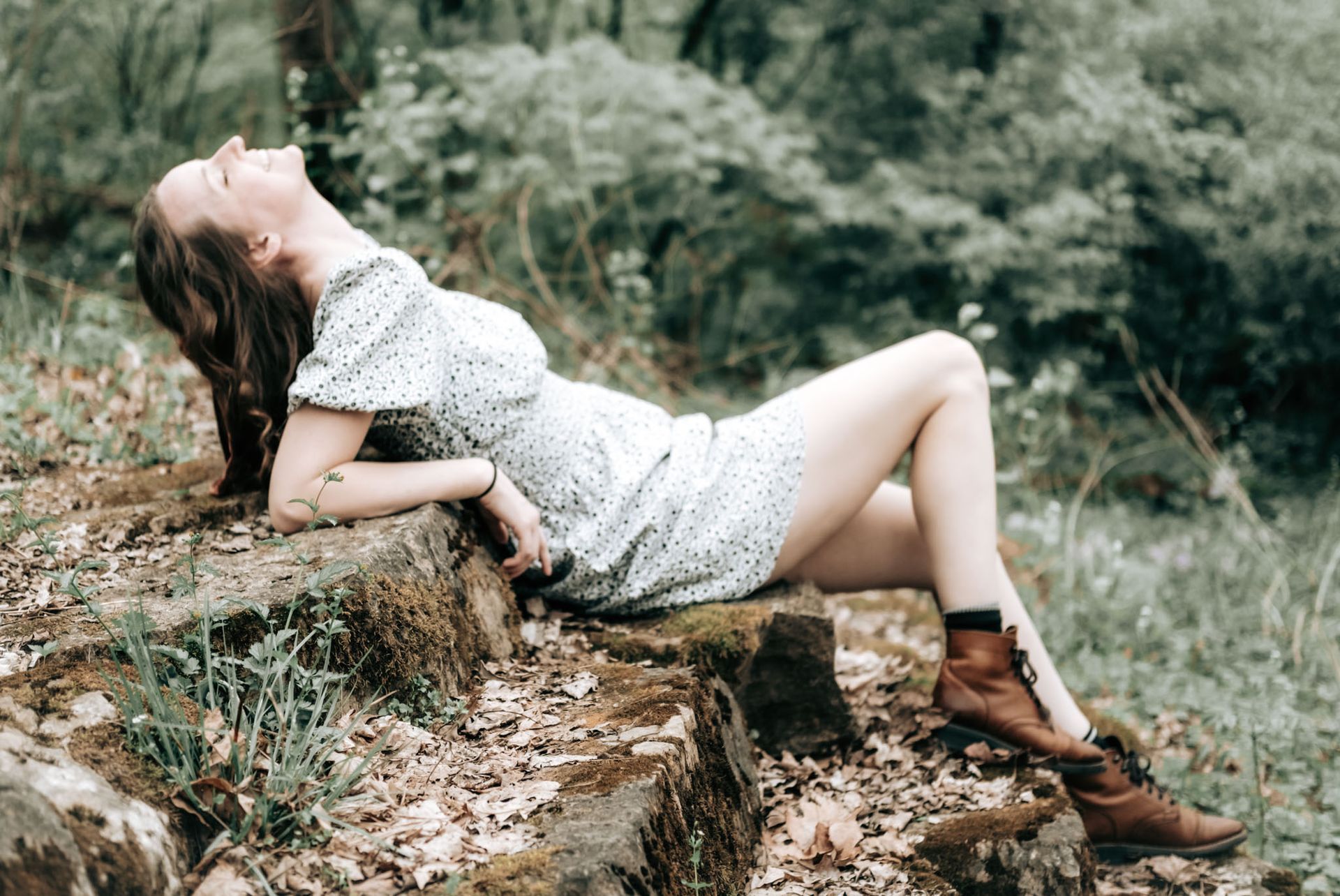 Woman in a white dress reclining on a rock in a wooded outdoor setting