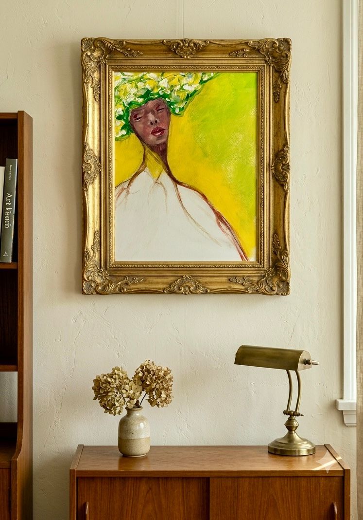 Framed abstract portrait above a wooden sideboard with lamp and dried flowers