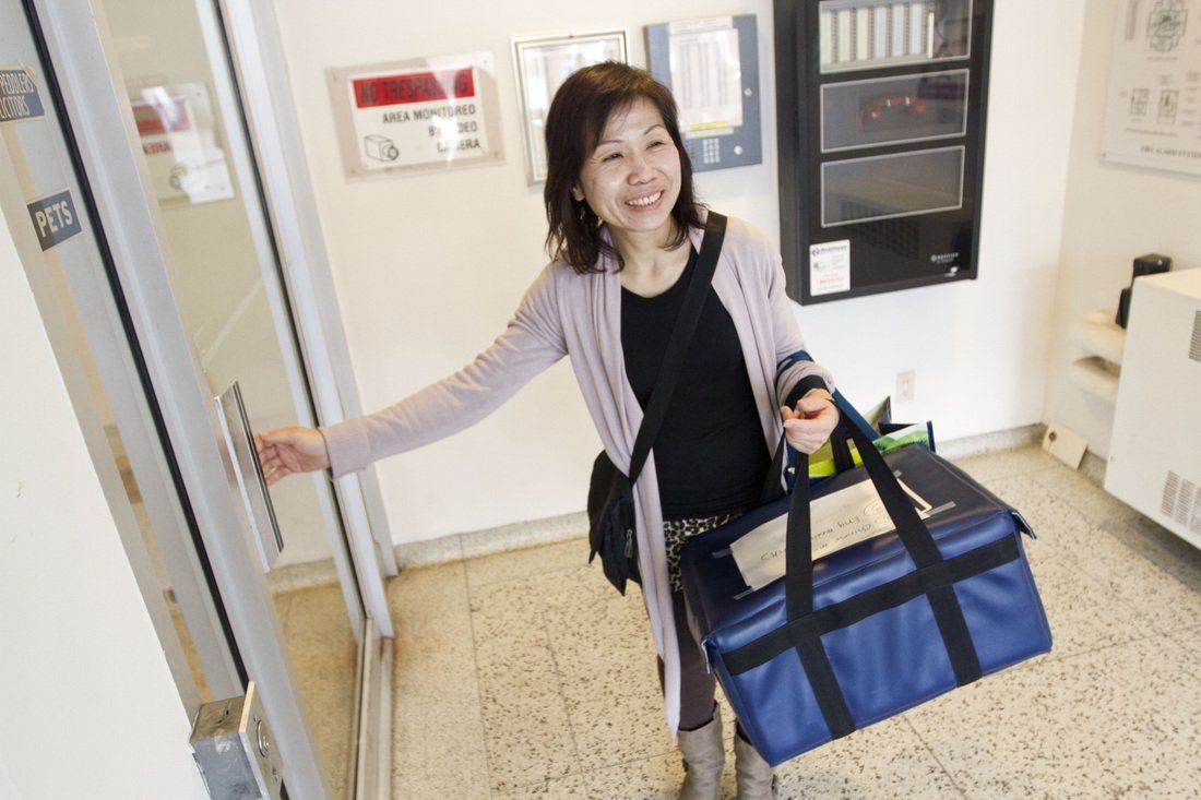 A woman is standing in front of an elevator holding a blue bag.
