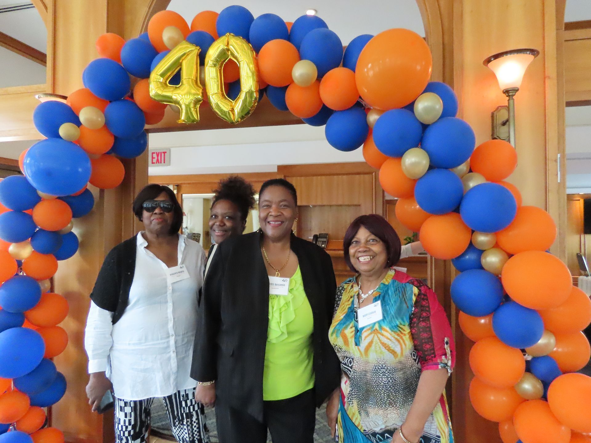 Three women are posing for a picture in front of a balloon arch with the number 40 on it