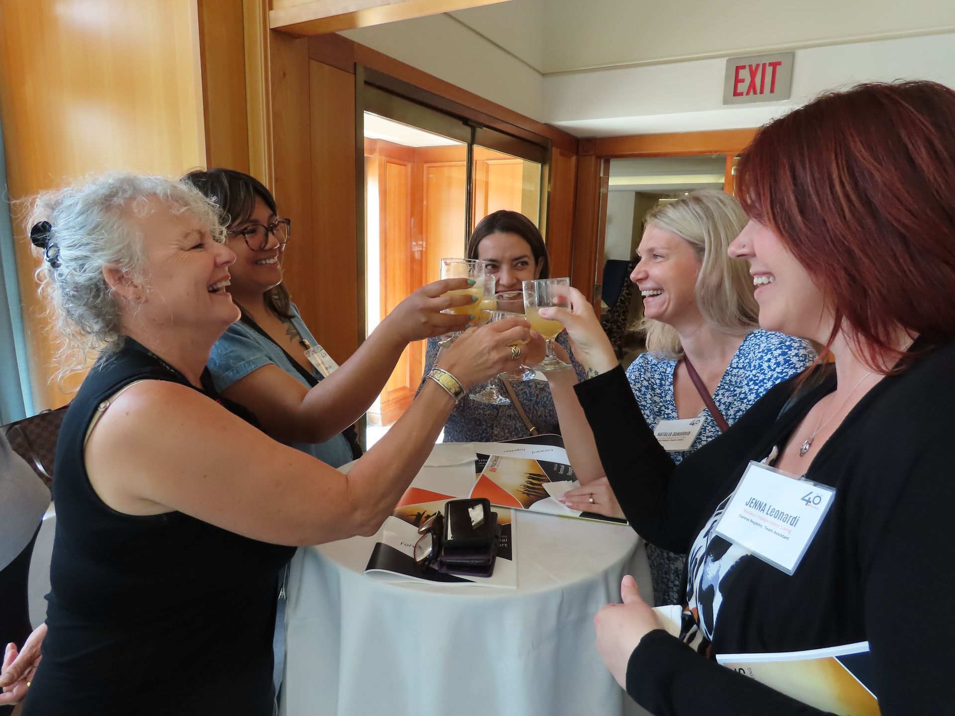 A group of women are toasting with champagne in front of an exit sign