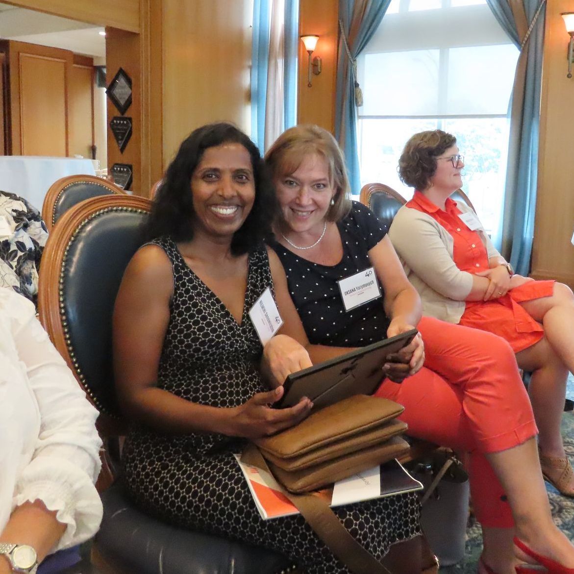 A group of women are sitting in chairs with one woman holding a tablet