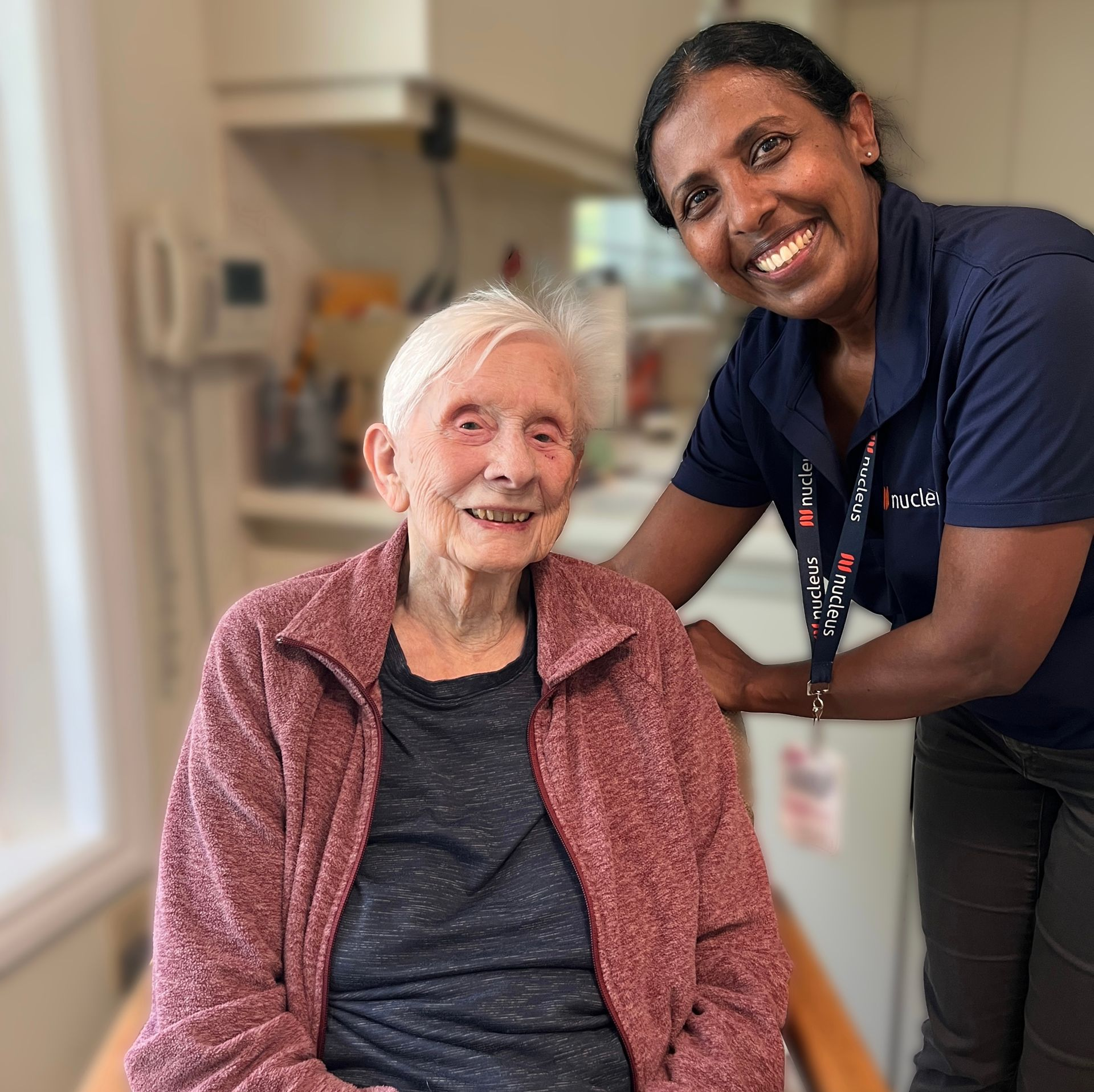 A nurse is holding the hand of an elderly woman in a living room.