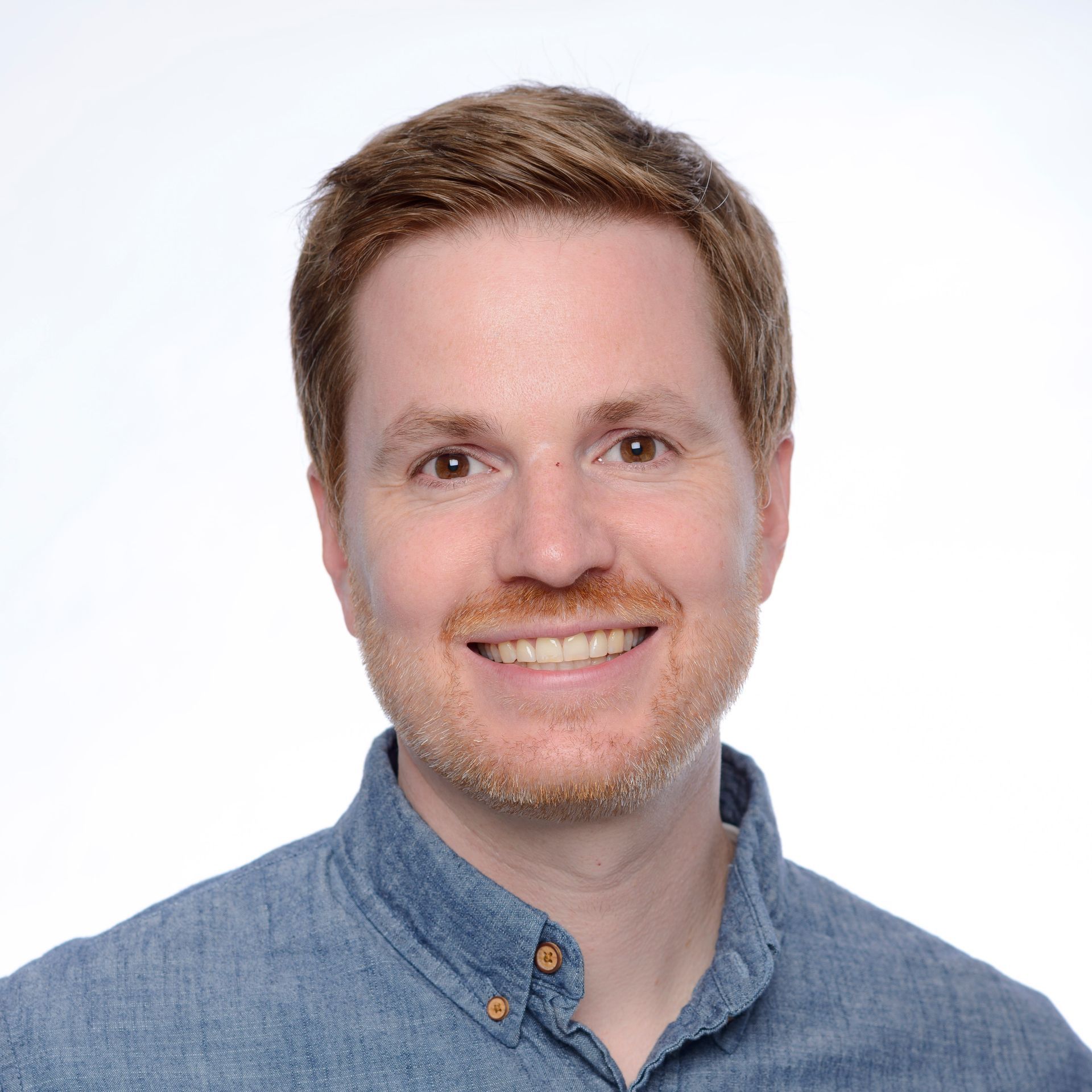 A man with a beard is smiling for the camera in a hallway.