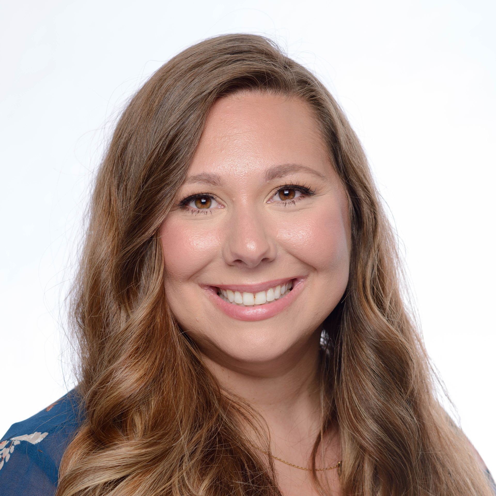 A woman wearing a pink jacket and a necklace is smiling for the camera.