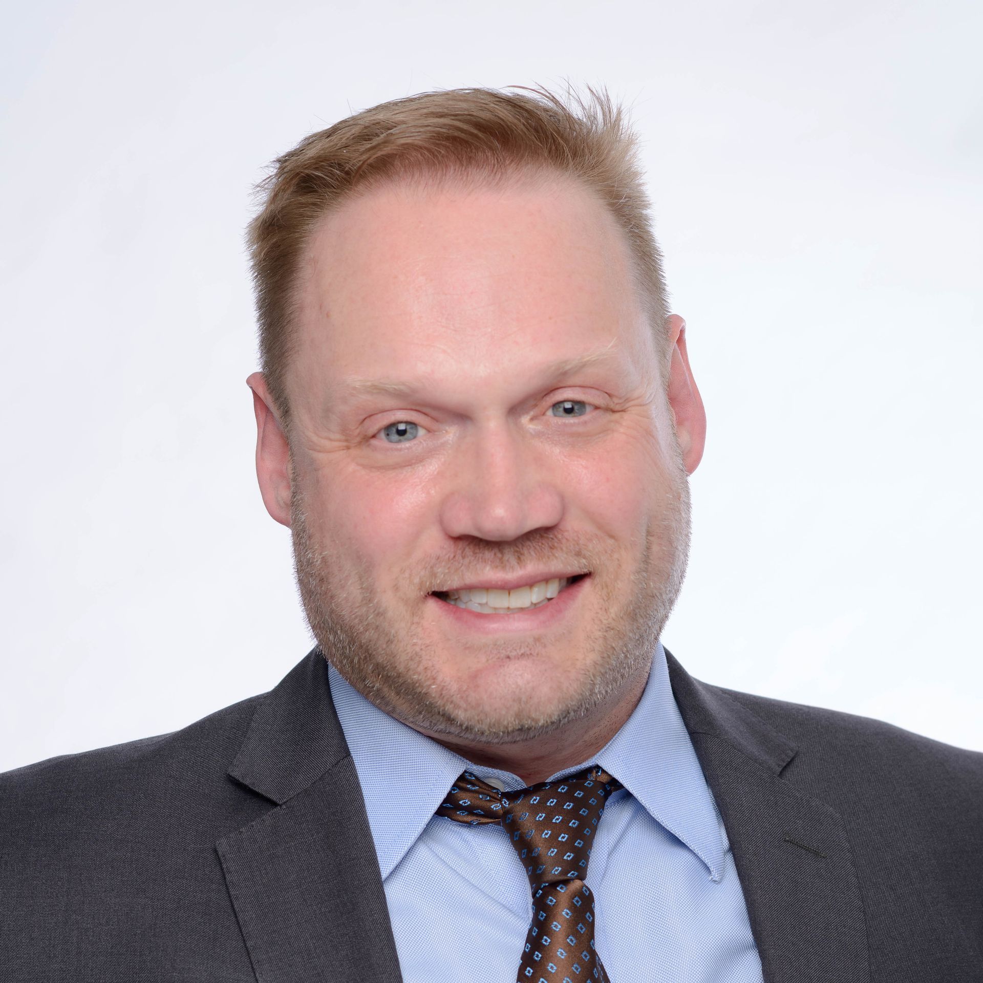 A man in a blue shirt and red tie looks at the camera