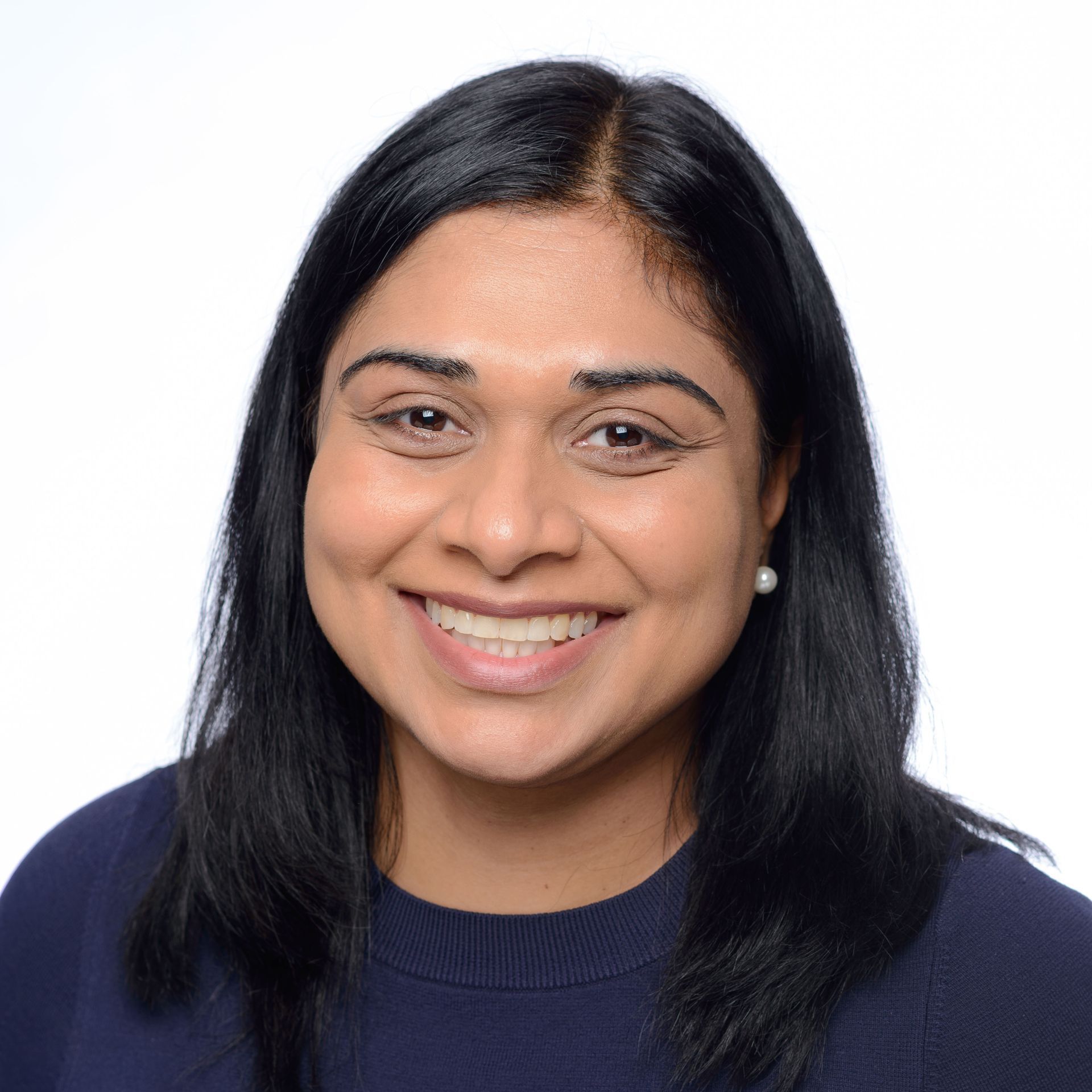 A woman wearing a pearl necklace and a tan jacket is smiling for the camera.