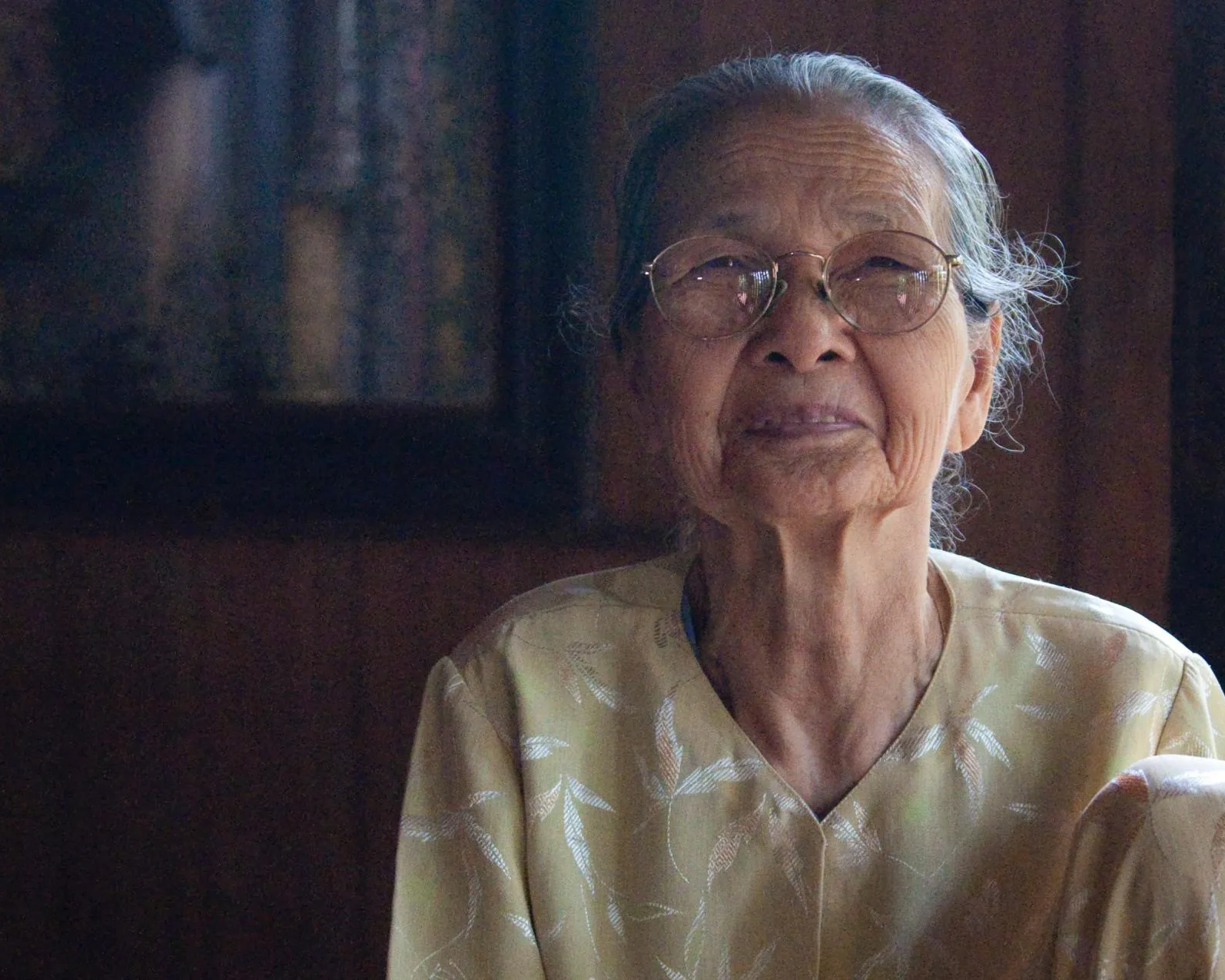 A close up of an elderly woman wearing glasses and a yellow shirt.