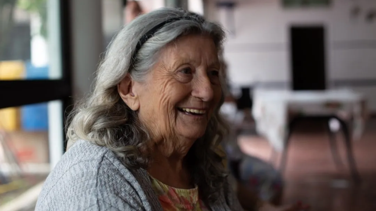 A close up of an elderly woman smiling in a room.