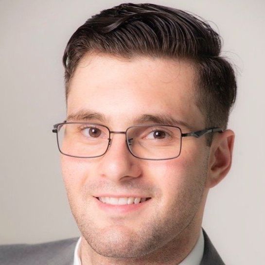 A man wearing glasses and a suit is smiling for the camera.