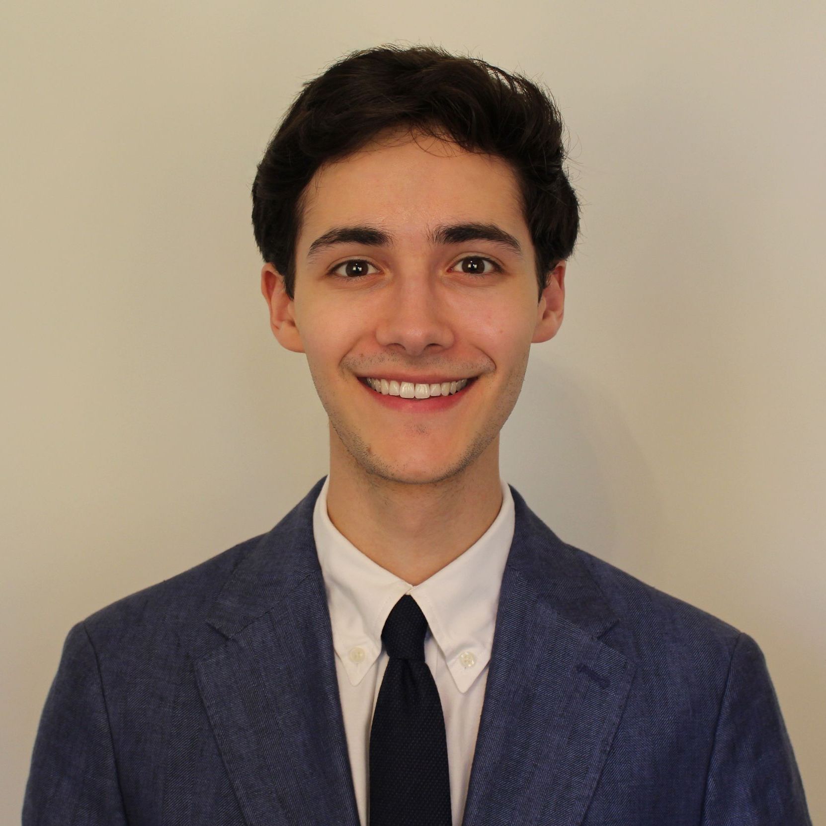 A young man in a graduation cap and gown is smiling in front of a building.