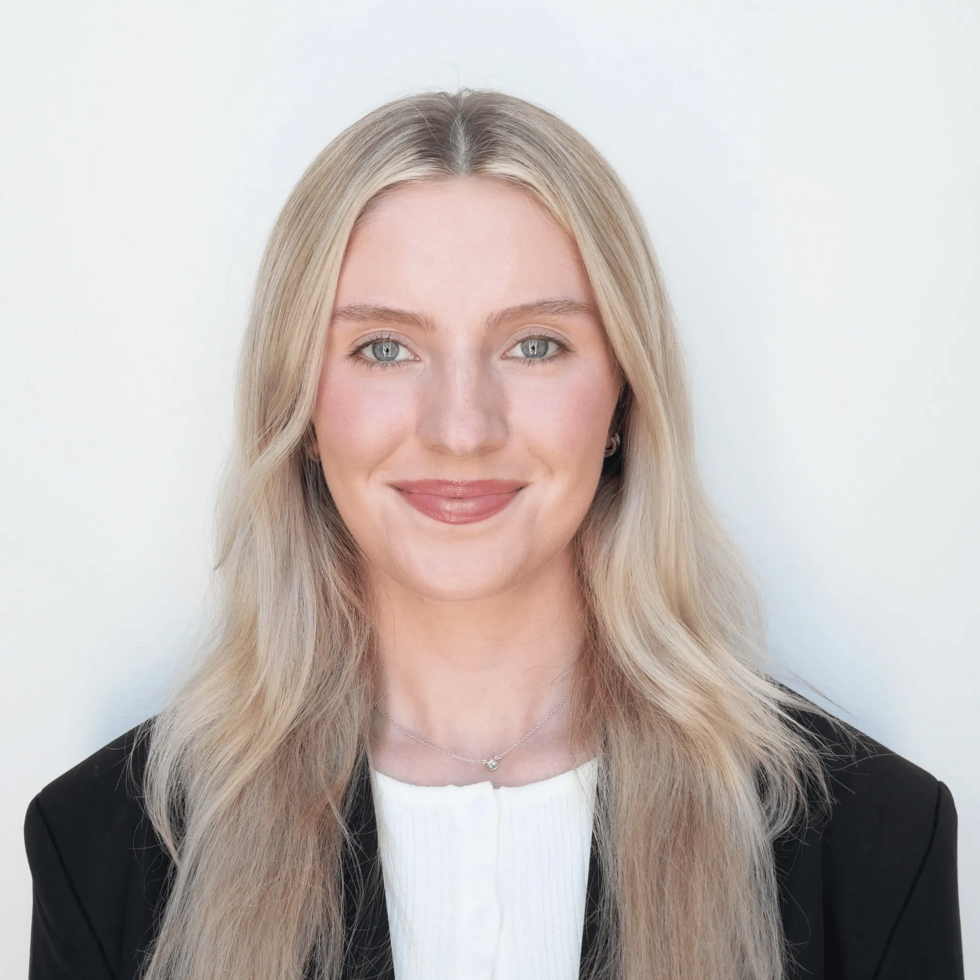 A young woman wearing a white shirt and black blazer is smiling for the camera.