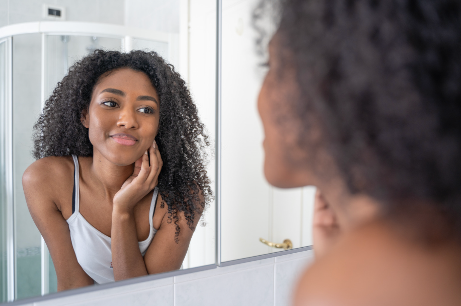 A woman is looking at her reflection in a bathroom mirror.