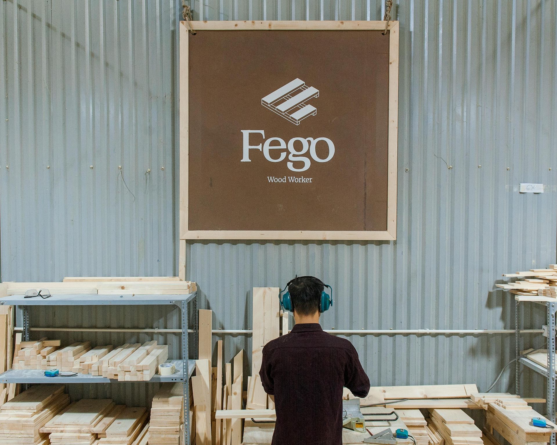 Person in workshop wearing ear protection, working with wood. Fego logo on wall. — Serena's Local Cleaning Company In Toowoomba, QLD