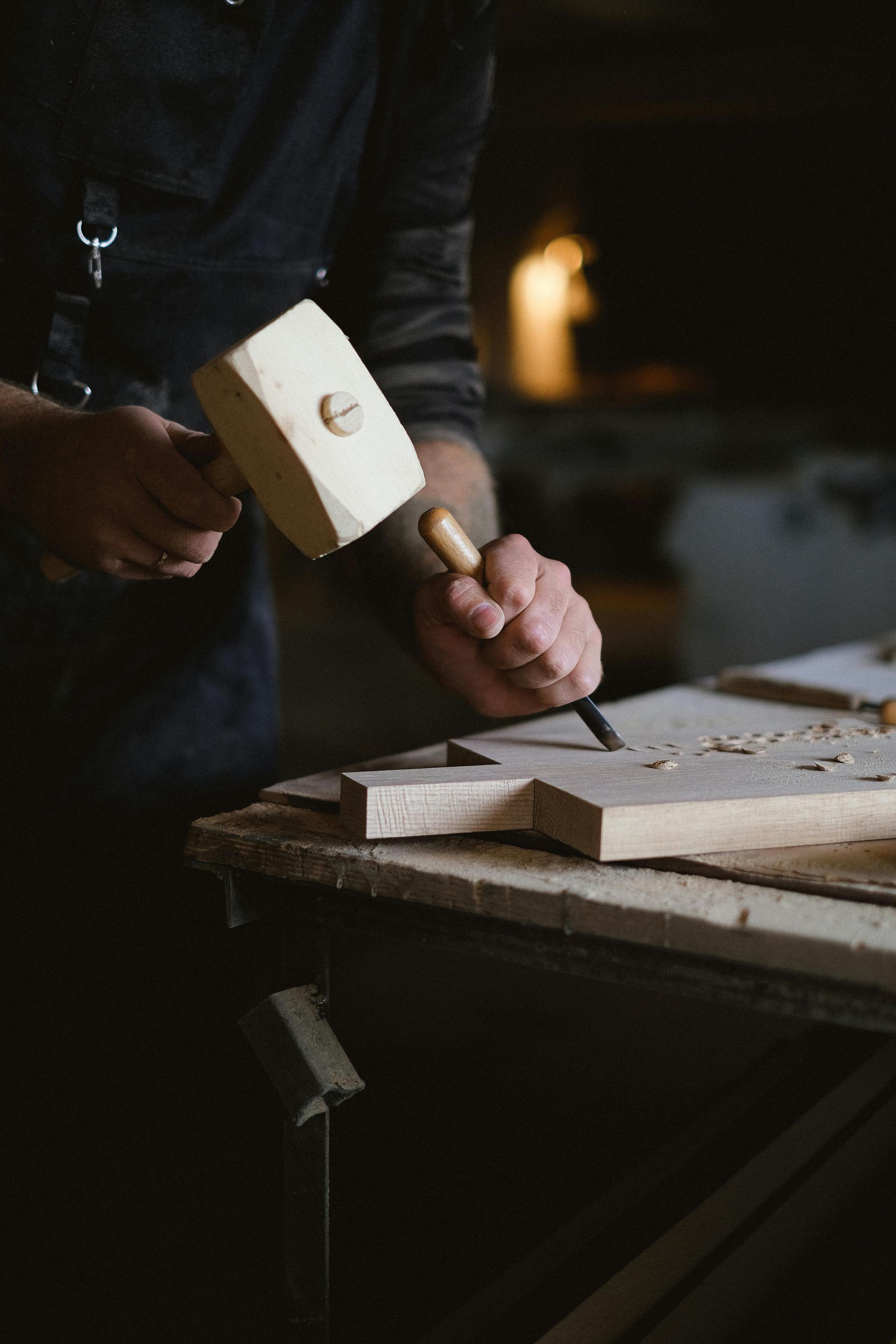 Person chiseling wood with a mallet and chisel on a workbench. Dark setting. — Serena's Local Cleaning Company In Toowoomba, QLD