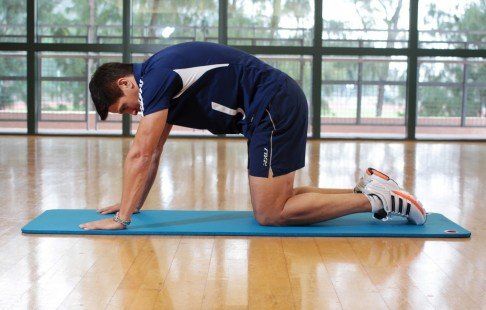 A man is kneeling on a yoga mat in a gym.