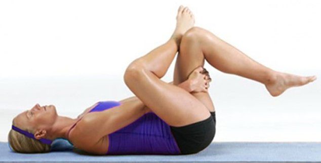 A woman is laying on her back on a yoga mat with her legs crossed.