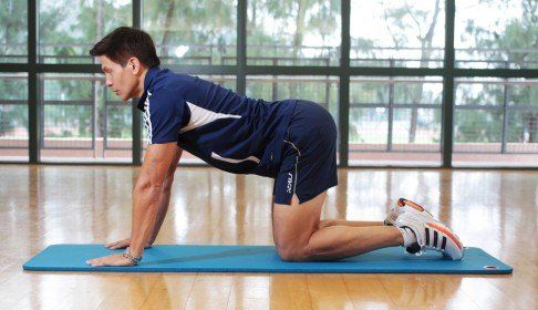 A man is kneeling on a yoga mat in a gym.