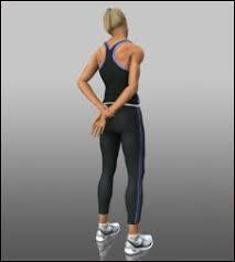 A woman in a black tank top and black leggings is standing with her hands behind her back.