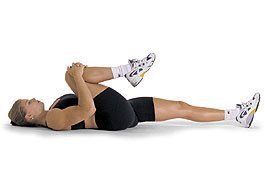 A woman is laying on her stomach stretching her leg.