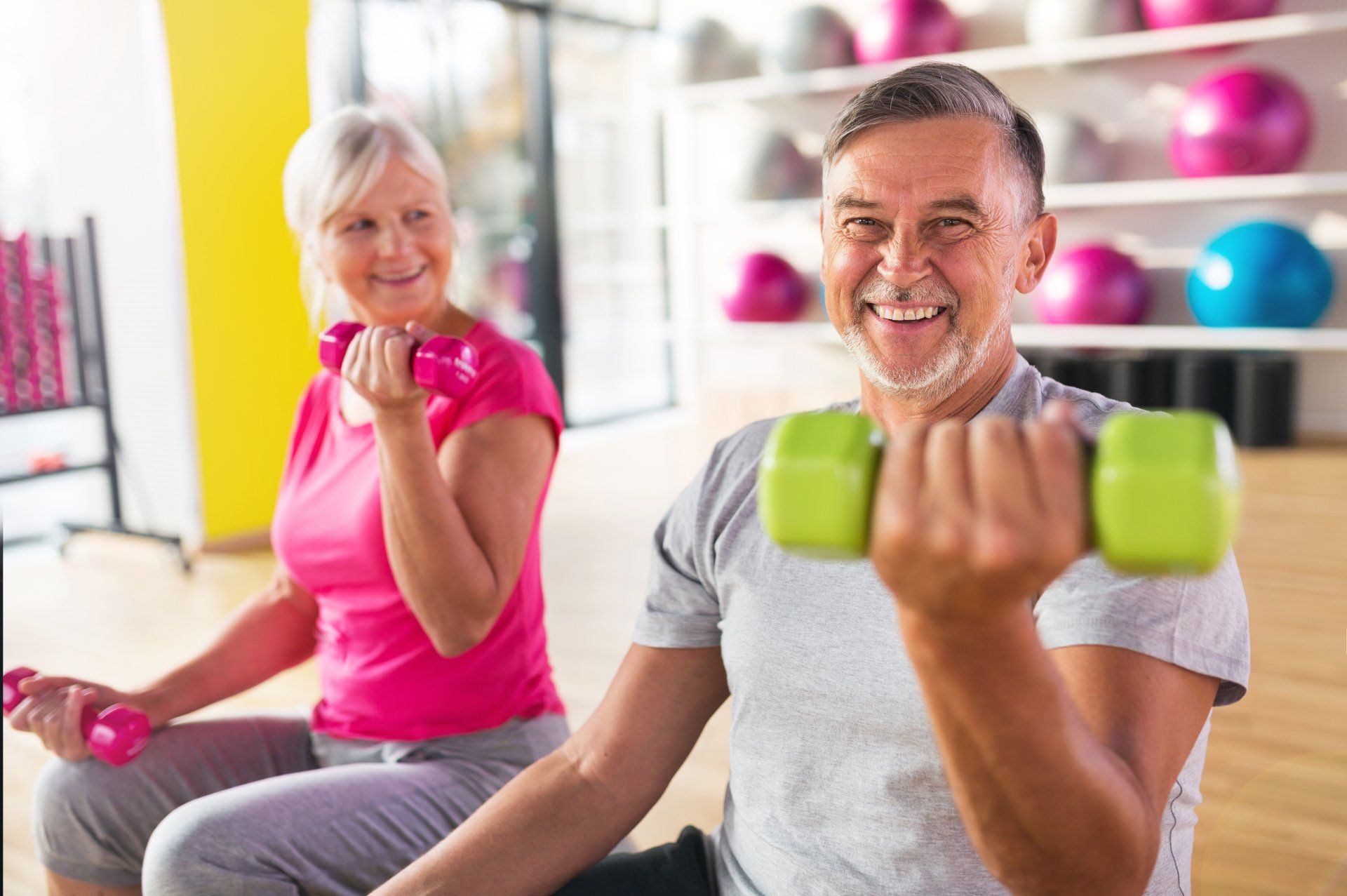 A man and a woman are lifting dumbbells in a gym.