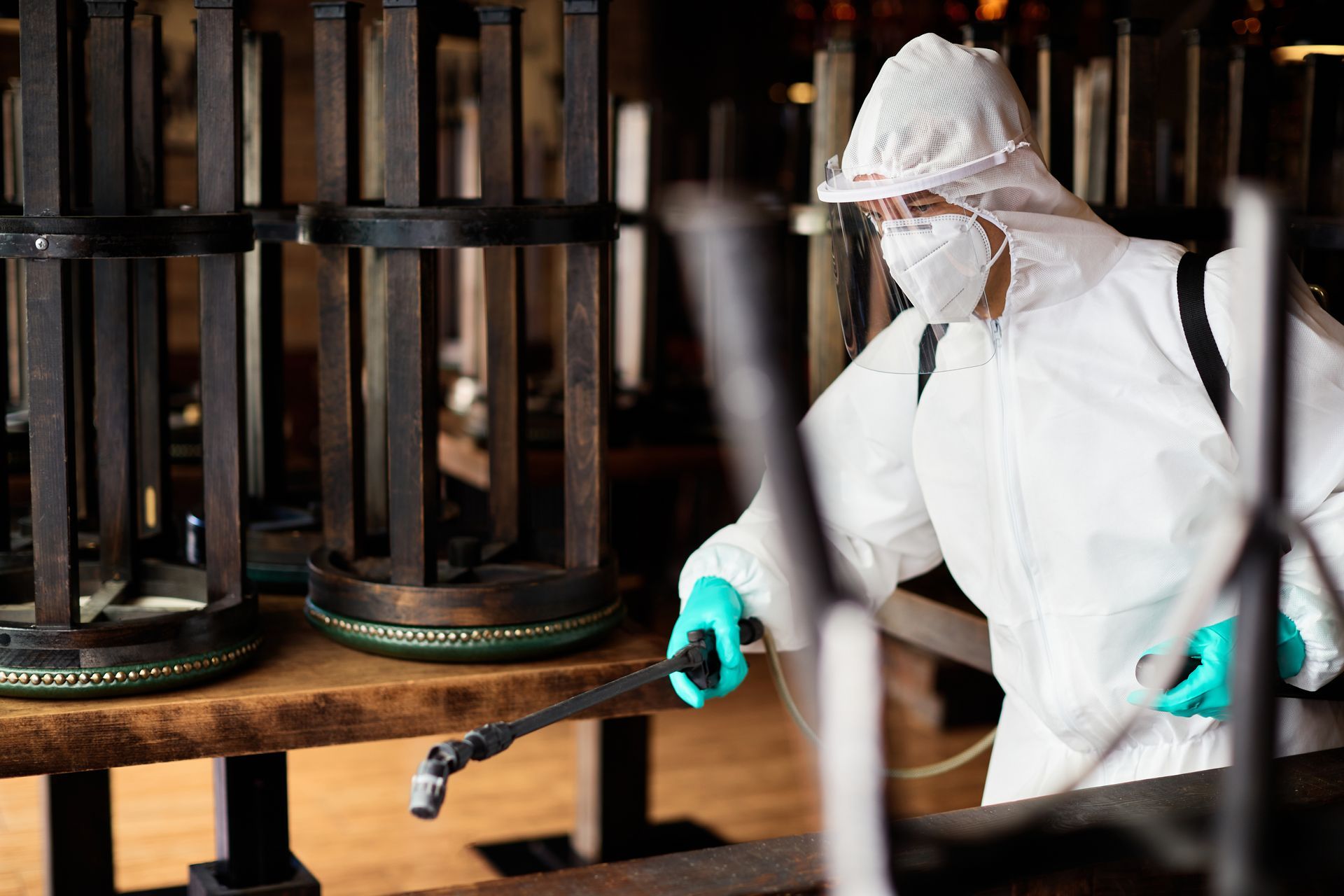 A man in a protective suit is spraying a table in a restaurant.