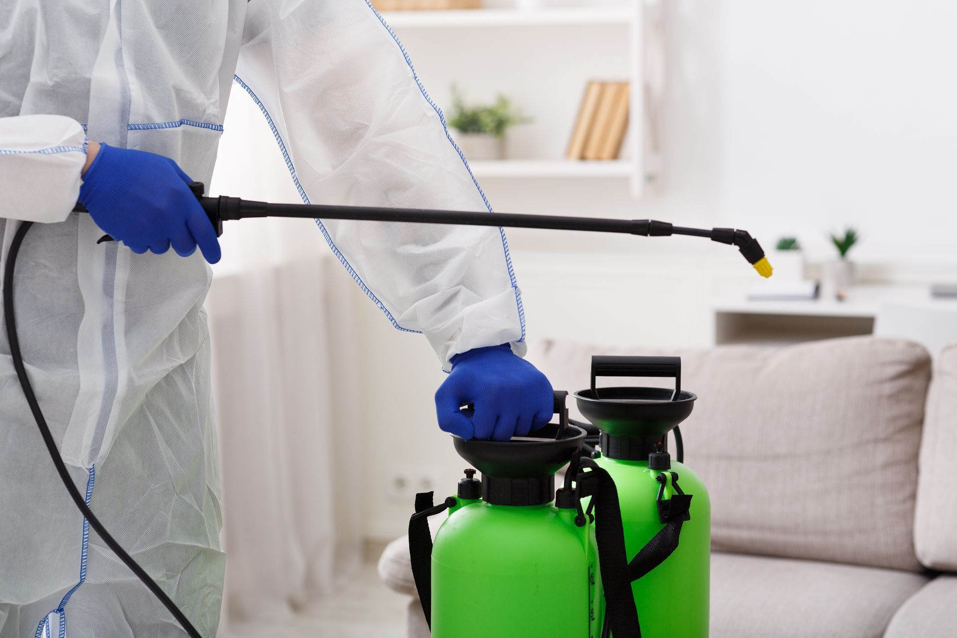 A person in a protective suit is spraying a room with a sprayer.