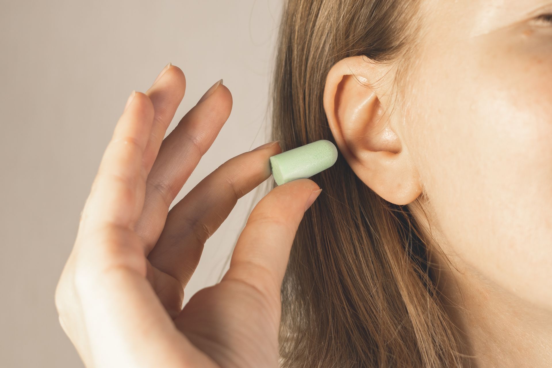 Person inserting a green earplug into an ear