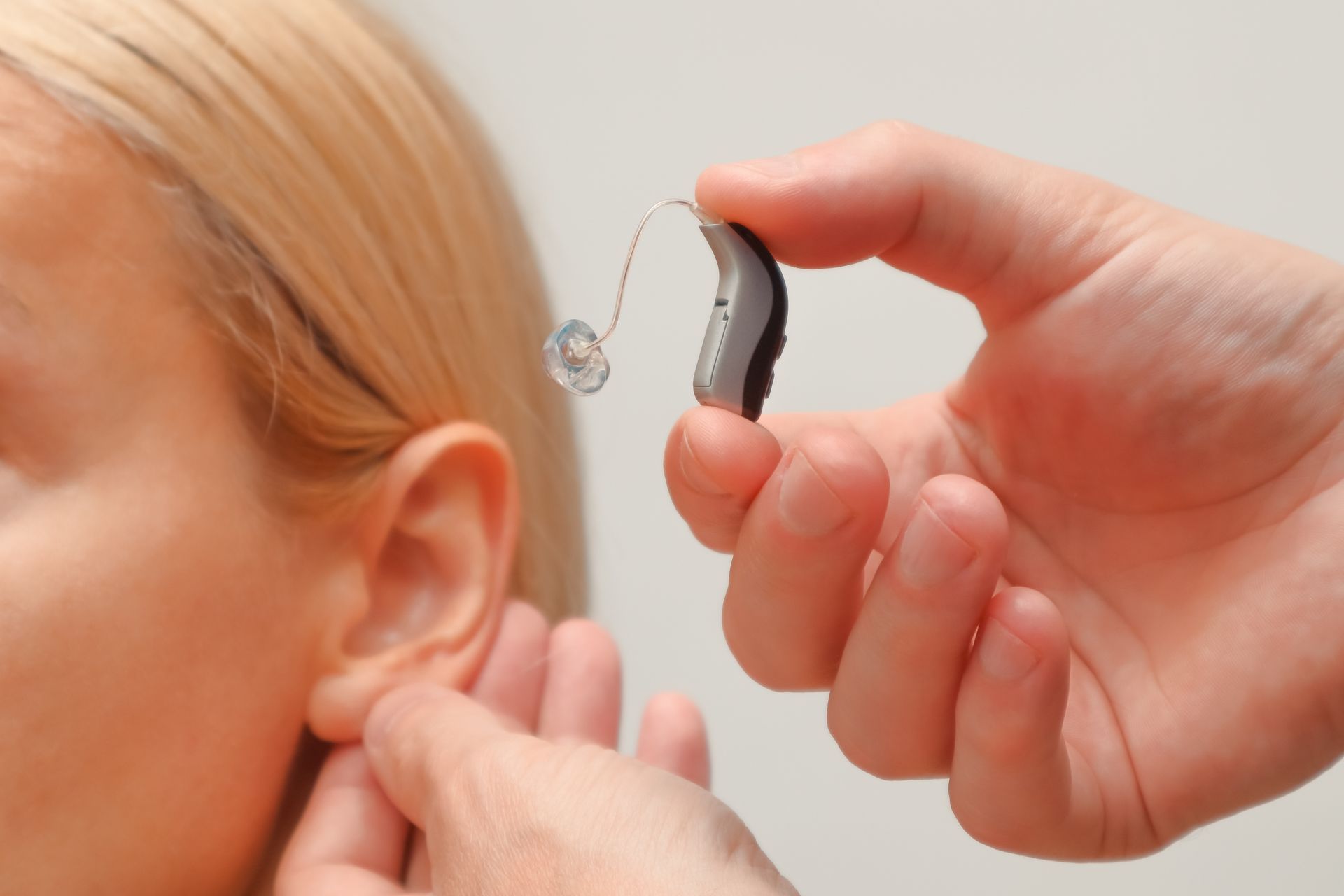 Hearing aid being placed behind a person's ear by another hand